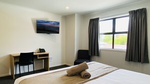 A hotel room with a bed, a desk, a chair, a TV on the wall, and a window with curtains. - Norton Motel (Hamilton)