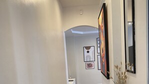 A hallway with a wooden floor, white walls, and a black console table with a candle and a vase. - Bel Appartement à 12min de Paris (Colombes)