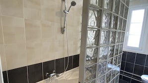A modern bathroom with a freestanding bathtub, black and beige tiled walls, and a glass shower enclosure. - Bel Appartement à 12min de Paris (Colombes)