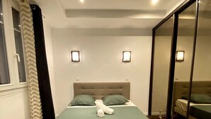 A bedroom with a bed, two bedside lamps, a window with curtains, and a mirror on the wall. - Bel Appartement à 12min de Paris (Colombes)