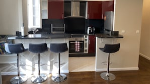 A modern kitchen with a central island, bar stools, and a refrigerator. - Bel Appartement à 12min de Paris (Colombes)