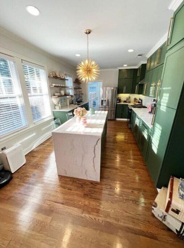 A modern kitchen with a marble island, green cabinets, and a pendant light.