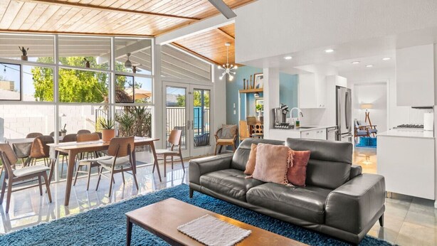 A modern living room with a leather sofa, a coffee table, and a dining area with chairs and a table. - Stylish Scottsdale Home W/ Pool Heating! (Scottsdale)