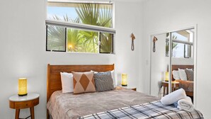 A bedroom with a bed, two bedside tables, a large window with a view of palm trees, and a mirror. - Stylish Scottsdale Home W/ Pool Heating! (Scottsdale)