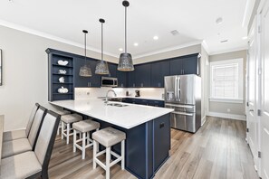 A modern kitchen with dark blue cabinets, a white island with bar stools, stainless steel appliances, and pendant lighting. - Ocean Pearl | Newly Built | Pool | Beach Access | My Beach Getaways (Gulf Shores)
