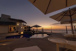 A pool area with umbrellas, lounge chairs, and a view of the ocean at sunset. - Beachfront Villa with Heated Pool (La Paz)