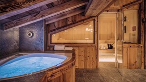 A wooden cabin with a hot tub, sauna, and a stone wall.