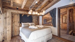 A cozy bedroom with a wooden ceiling, a large bed with white linens, and a modern chandelier.