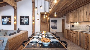 A modern kitchen with wooden cabinetry, a marble countertop, and a dining area with a long table set for six.