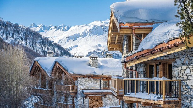 A mountain lodge with stone and wood architecture, multiple balconies, and snow-covered surroundings.