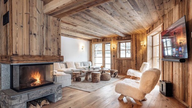 Interior acogedor de una cabaña de madera con chimenea de piedra, asientos mullidos y un televisor montado.