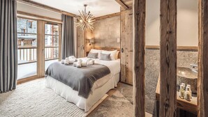 Un dormitorio con una cama grande, vigas de madera, una pared de piedra y vistas a un edificio de piedra.