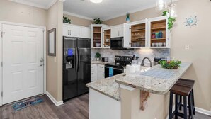 Una cocina moderna con armarios blancos, un refrigerador de acero inoxidable, un microondas y una encimera de granito.