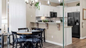Una cocina moderna con armarios blancos, un refrigerador negro y una zona de comedor con una mesa redonda y sillas.