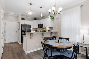 A modern kitchen with white cabinets, a central island, and a dining area with a round table and chairs.