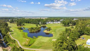 Un campo de golf con un estanque, árboles y un pueblo al fondo.