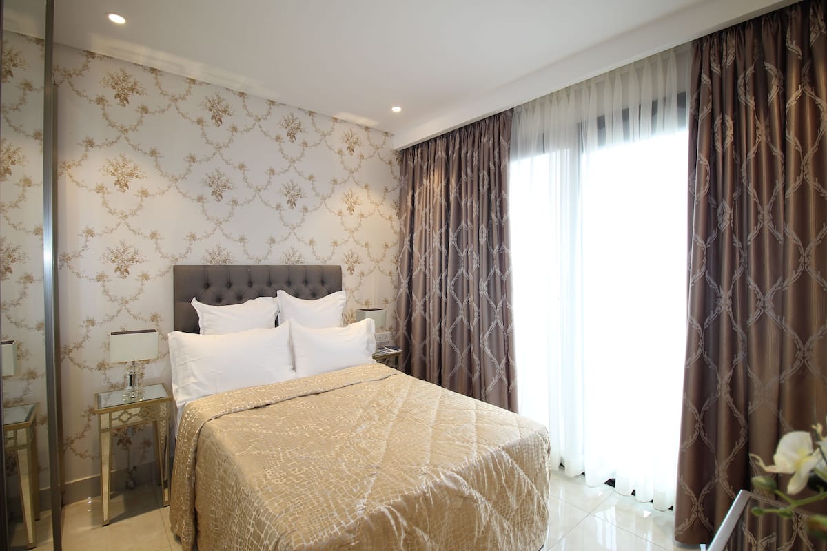 A hotel room with a large bed, a nightstand, a mirror, and a window with curtains.