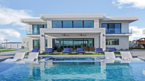 Un bâtiment moderne à deux étages, doté d’une piscine et de chaises longues.