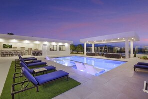 Un área de piscina moderna al aire libre con sillones de descanso y un espacio de estar techado.