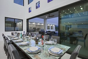 Comedor con una larga mesa dispuesta para una comida, ventanas grandes y vistas al exterior.