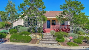 A two-story house with a red front porch, stone steps leading to the door, and a well-maintained garden with various shrubs and a small pond. - Lovely Home- near fine dining and pool area (Bret Harte Cottage) (Angels Camp)