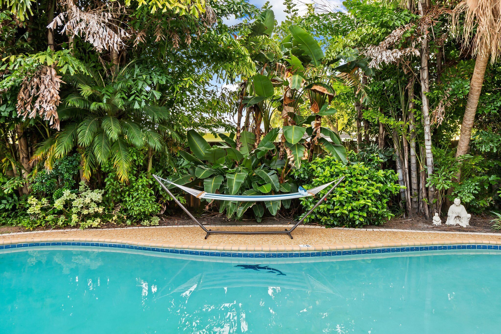 Une piscine avec un hamac et une statue, le tout situé dans un jardin luxuriant.