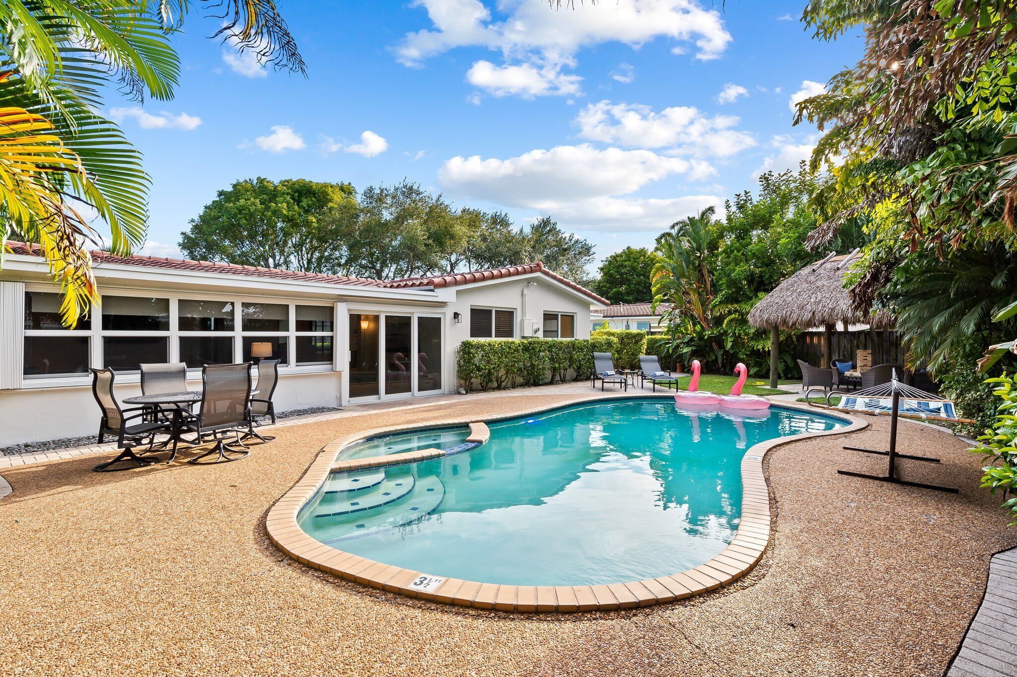 A swimming pool with a curved edge, surrounded by a pebble deck, and a patio area with outdoor furniture.