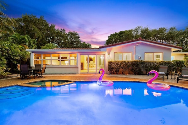 A modern house with a swimming pool, two flamingo floats, and outdoor furniture. - Retro 1950s Florida Home ~ Solar Heated Pool ~ Spa ~ Tiki Hut ~ Huge Backyard ~ Hammock ~ Two Bikes (Pompano Beach)