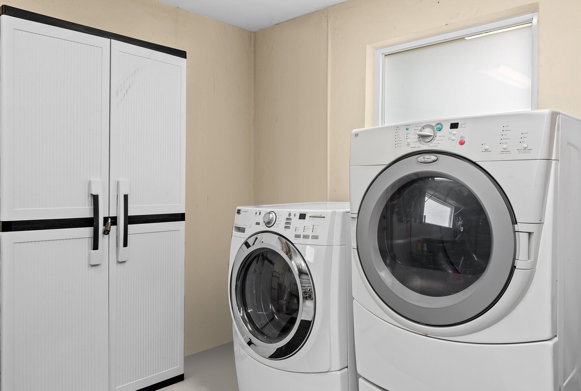 A laundry room with two white washing machines and a white wardrobe with black handles.