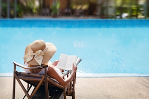 A person reading a book by a poolside chair.