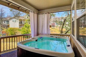 Un jacuzzi en una terraza de madera con vista a casas y árboles.