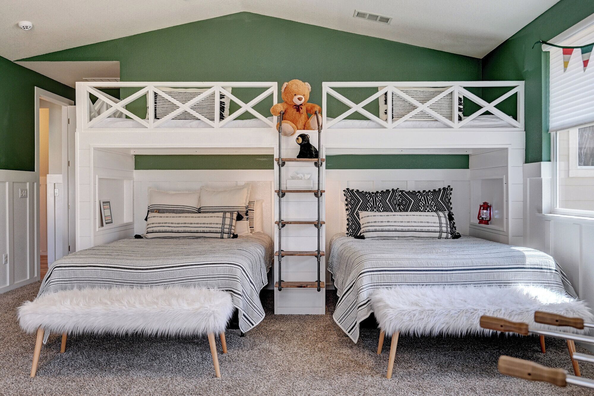 Ein Zimmer mit zwei Stockbetten, einer Leiter, einem Teddybären und einem kleinen Regal mit einer Laterne.