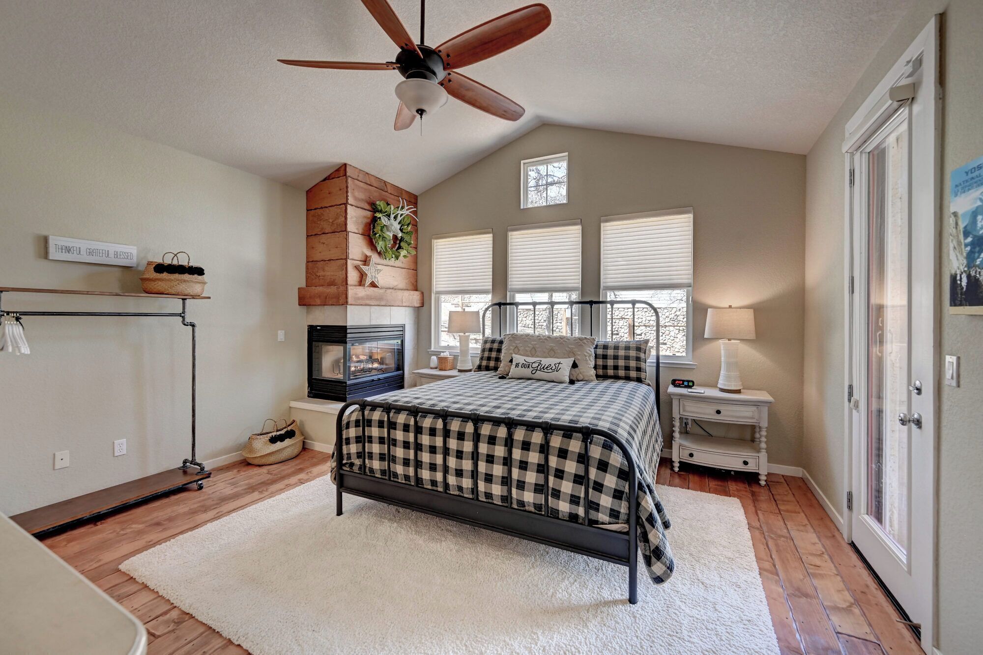 A bedroom with a bed, a fireplace, a ceiling fan, a window, and a door.
