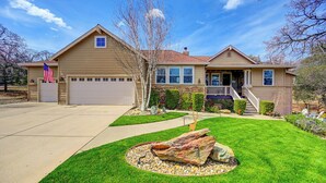 A two-story house with a garage, a front porch, and a well-maintained lawn with a decorative rock centerpiece. - Beautifully furnished home with HOT TUB (Angels Camp)