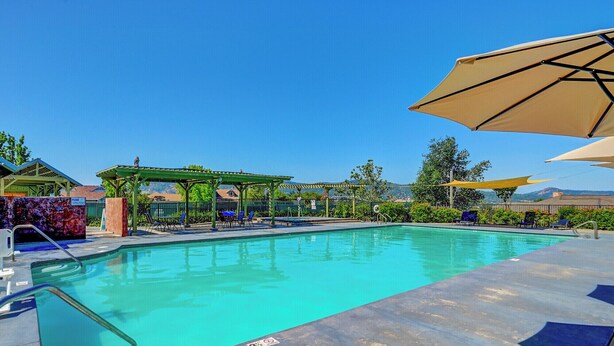 A swimming pool with lounge chairs and umbrellas, surrounded by greenery and a clear sky. - Raspberry Cottage-stunning view of golfcourse (Angels Camp)