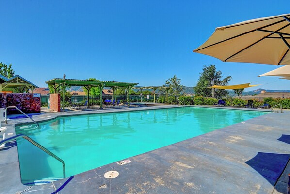 A swimming pool with lounge chairs and umbrellas, surrounded by greenery and a clear sky. - Raspberry Cottage-stunning view of golfcourse (Angels Camp)