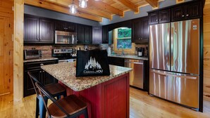 Cocina con armarios de madera oscura, electrodomésticos de acero inoxidable, una isla con encimera de granito y una lámpara colgante.