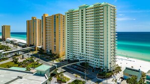 A high-rise hotel with multiple balconies, a beach view, and a pedestrian bridge. - GULF FRONT BEDROOM @ CELADON BEACH RESORT ~FREE Beach Chair Service! (Panama City Beach)