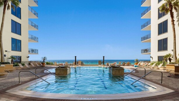 A pool area with two hot tubs, lounge chairs, and a view of the ocean.