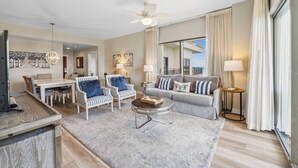 A spacious living room with a dining area, a balcony with a view, and a ceiling fan.