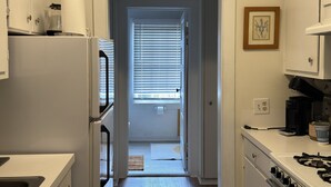 A kitchen with a refrigerator, stove, and a door leading to a hallway. - Wensel Cottage in downtown Natchez Walking distance to most shops & restaurants. (Natchez)