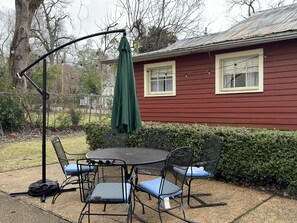 Eine Terrasse im Freien mit Tisch und Stühlen, einem grünen Sonnenschirm und einem roten Haus im Hintergrund.