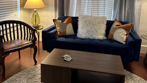A living room with a blue sofa, a wooden coffee table, a lamp, and a chair. - Wensel Cottage in downtown Natchez Walking distance to most shops & restaurants. (Natchez)