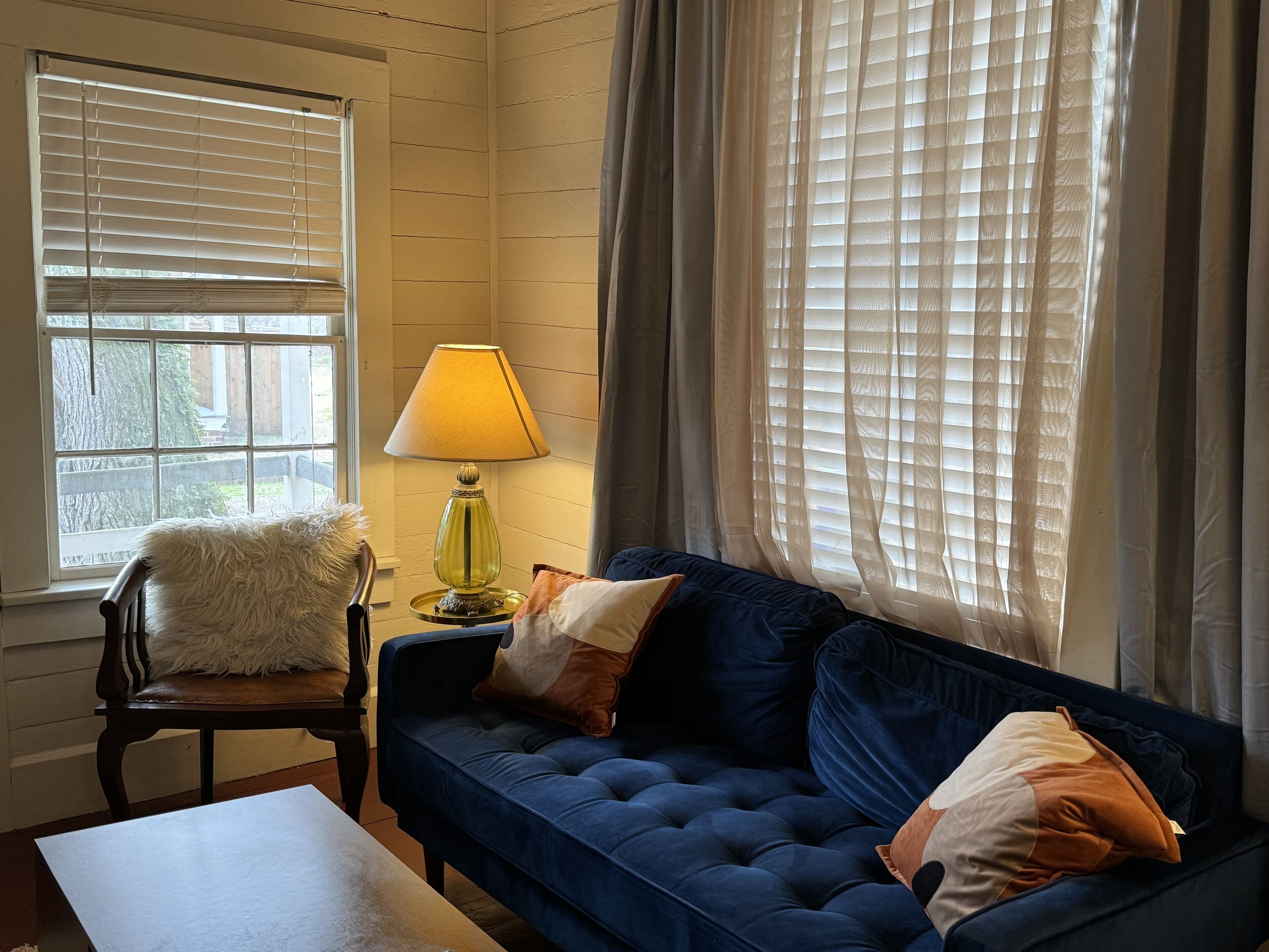 A cozy living room with a blue sofa, a fluffy chair, and a lamp on a side table.