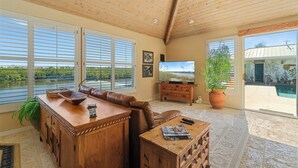 A spacious living room with a wooden ceiling, large windows, a television, a fireplace, and a view of the outdoors.