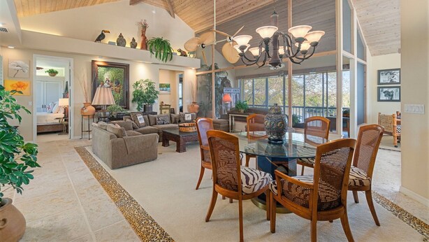 A spacious living room with a high ceiling, a dining area with a glass table and wicker chairs, and a cozy seating area with sofas and a fireplace.