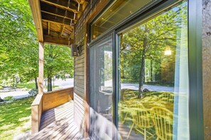 A wooden deck with a glass door leading to an outdoor area with a view of trees and a road.