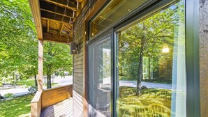 A wooden deck with a glass door leading to a view of a road and trees.