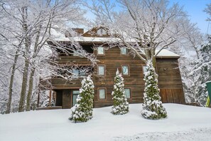 A wooden cabin with multiple windows, surrounded by snow-covered trees and a snow-covered roof.