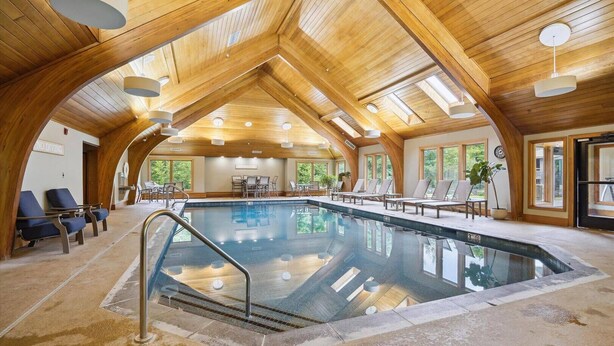An indoor swimming pool with wooden beams and a high ceiling, surrounded by lounge chairs and a 'No Diving' sign. - Charming Highridge Condo F2: Access to Pool, Hot Tub, and More! (Killington)